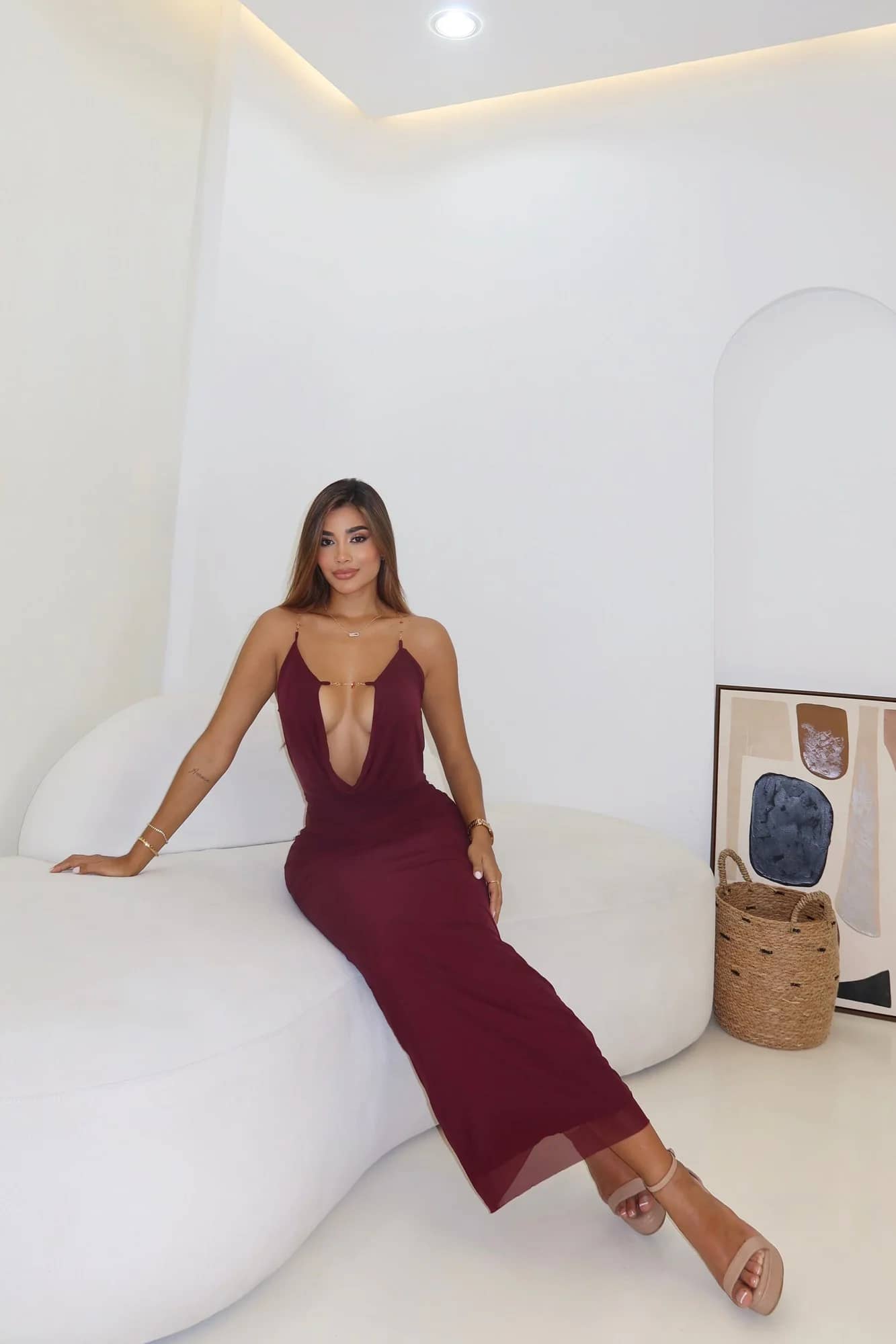 Modelo sentada luciendo el Vestido Flower vinotinto, maxi halter con escote en V profundo y tirantes de cadena dorada