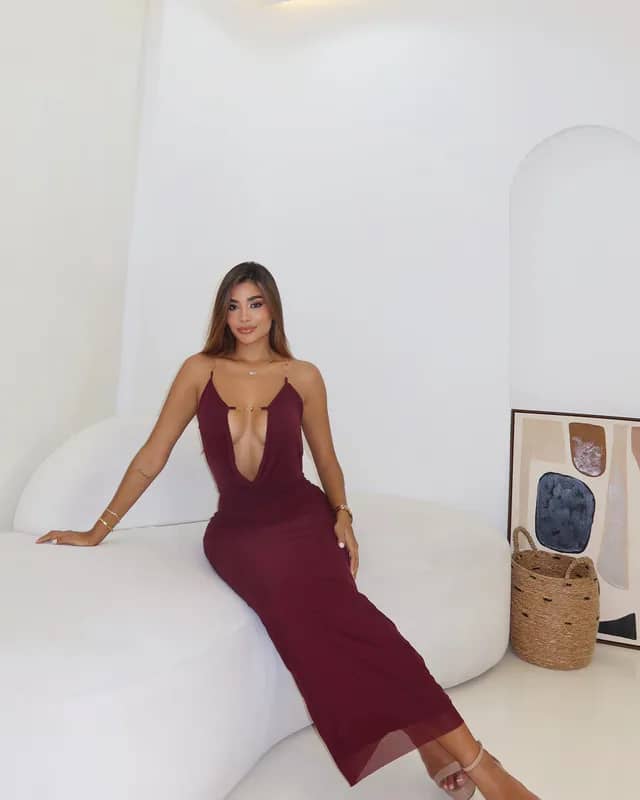Modelo sentada luciendo el Vestido Flower vinotinto, maxi halter con escote en V profundo y tirantes de cadena dorada