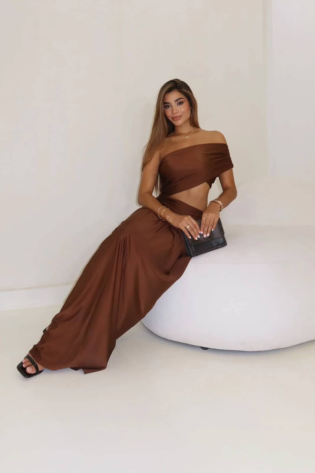 Modelo sentada con el Vestido Fantasía café: top drapeado a un hombro y abertura lateral