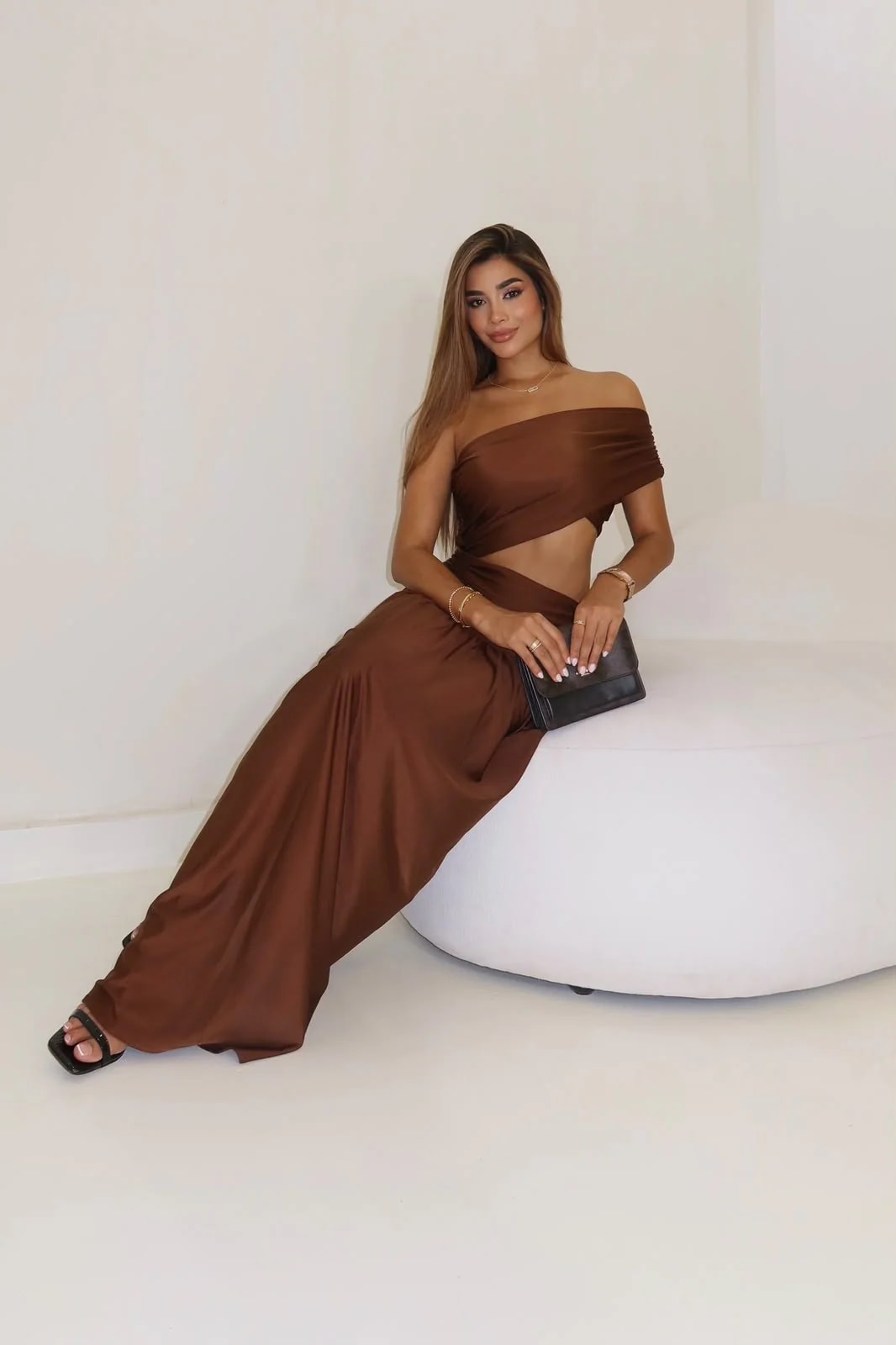 Modelo sentada con el Vestido Fantasía café: top drapeado a un hombro y abertura lateral